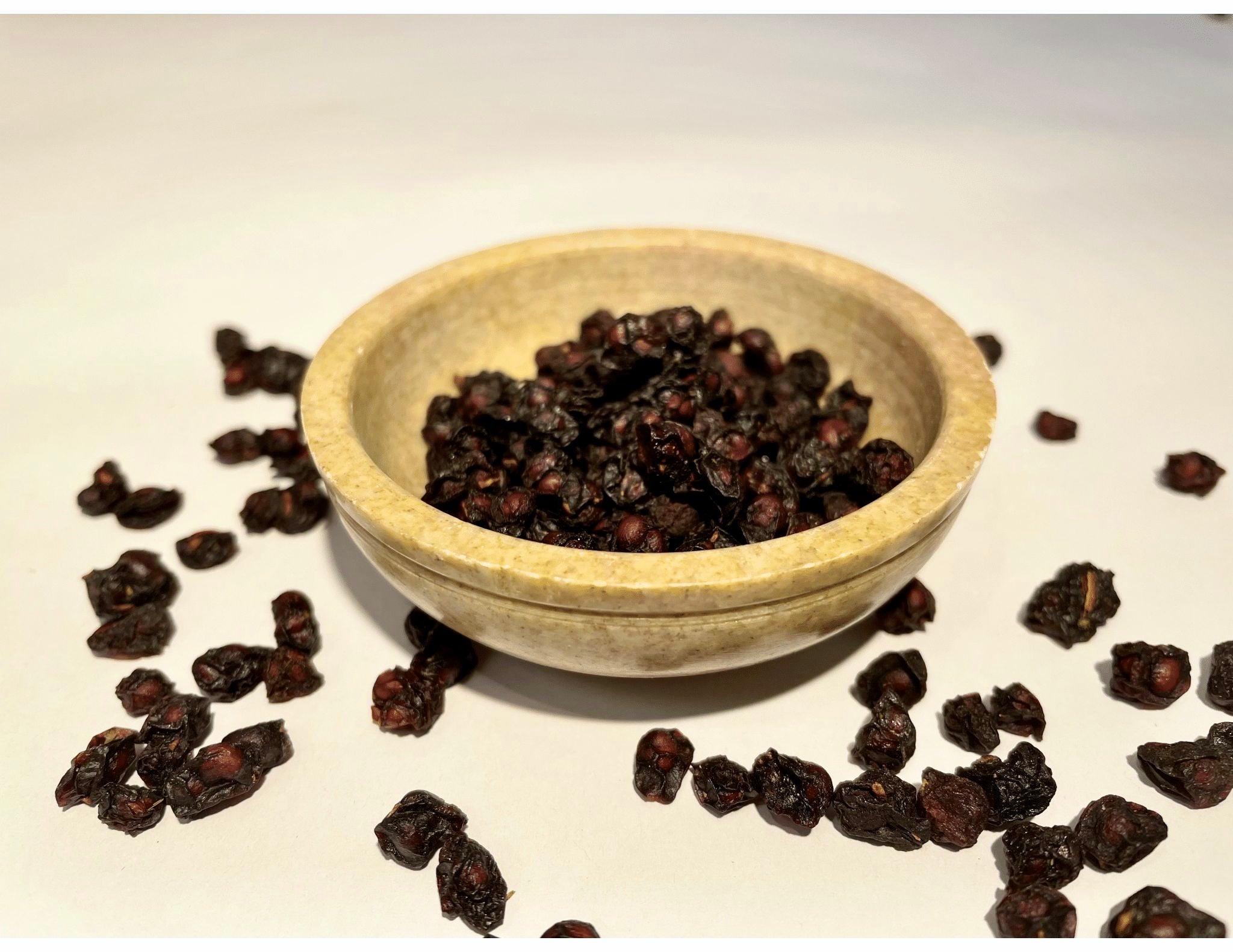 Dried Schisandra berries displayed in a bowl and scattered on a white surface